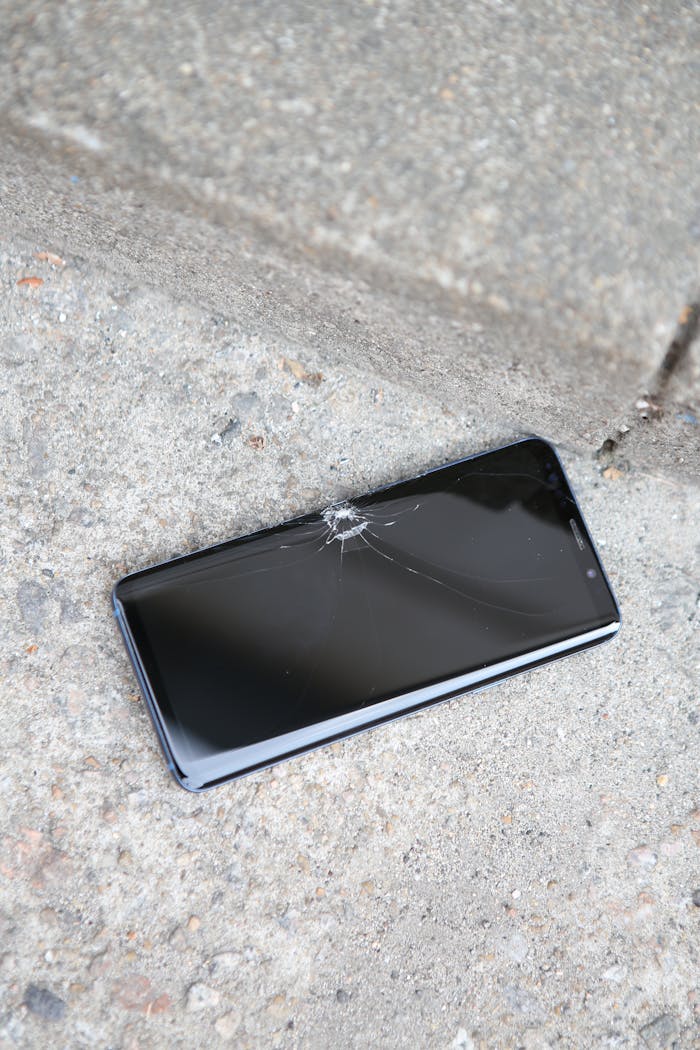 A cracked smartphone lying on a concrete pavement outdoors, ideal for concept of technical issues.