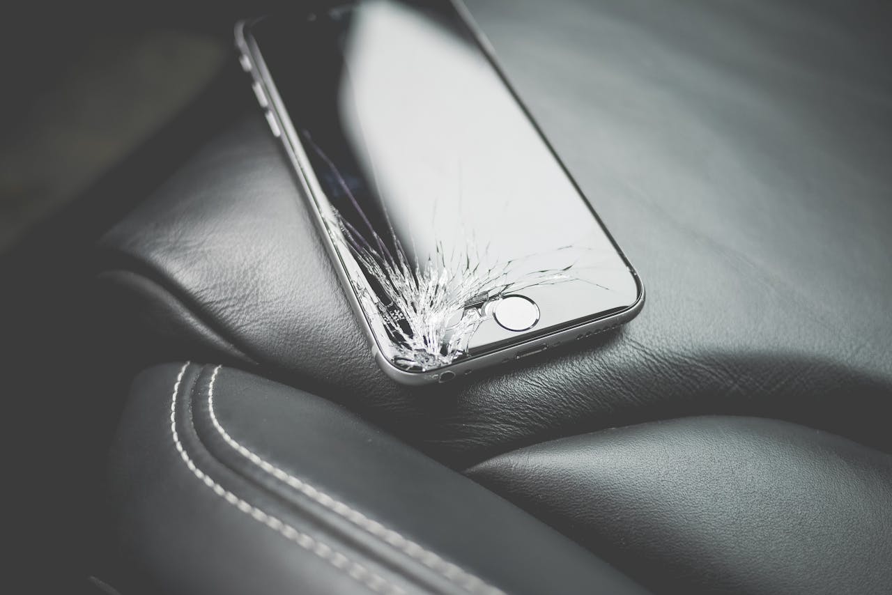 Close-up of a broken smartphone with a cracked screen on a leather car seat.